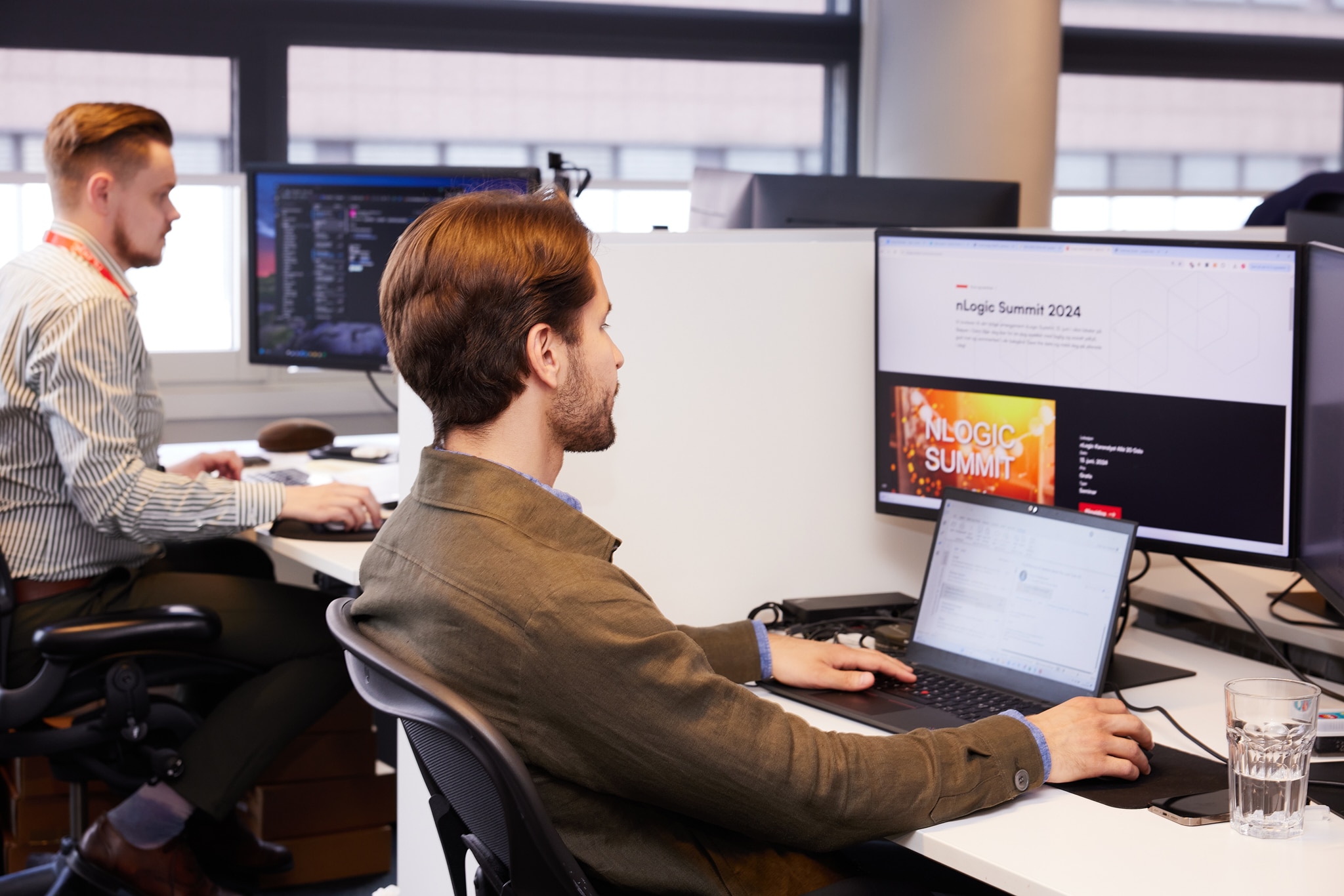 To menn foran skjermer i kontorlandskap.