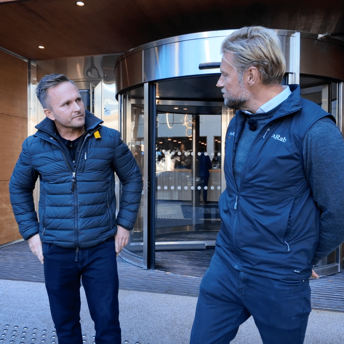 To menn prater sammen foran en inngang.